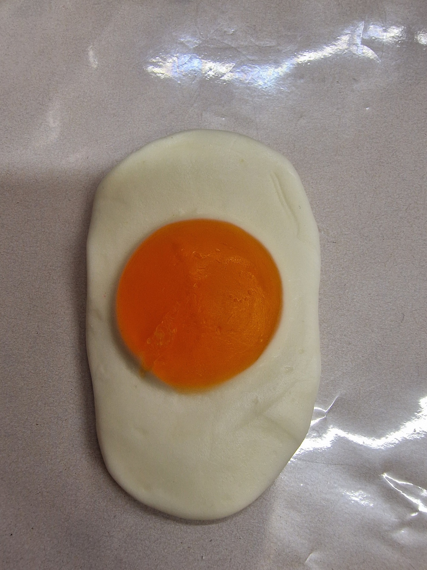 Ovo estrelado artificial com clara branca e gema laranja em fundo brilhante