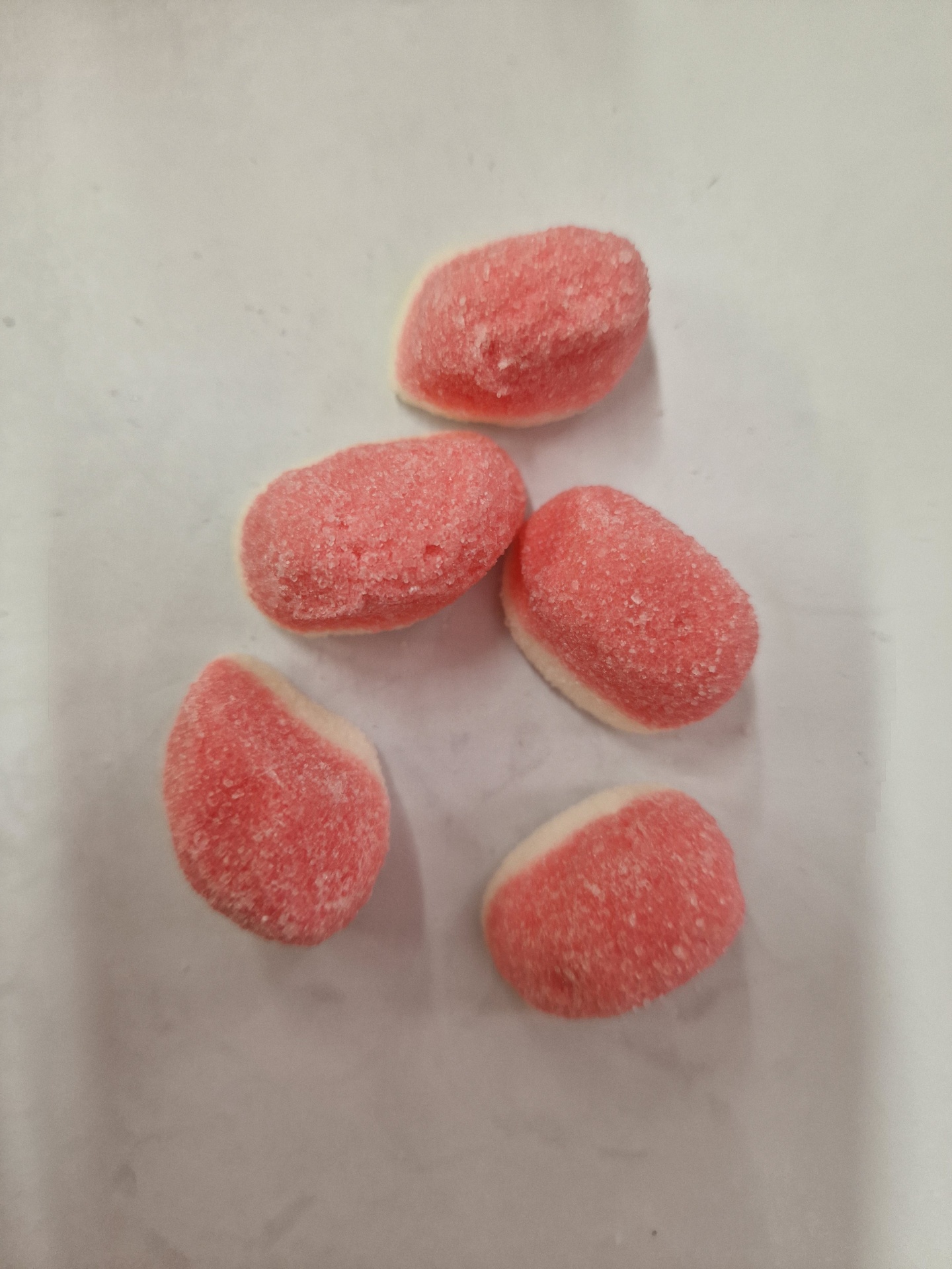 Cinco gomas de doce rosa e branco cobertas de açúcar em fundo branco