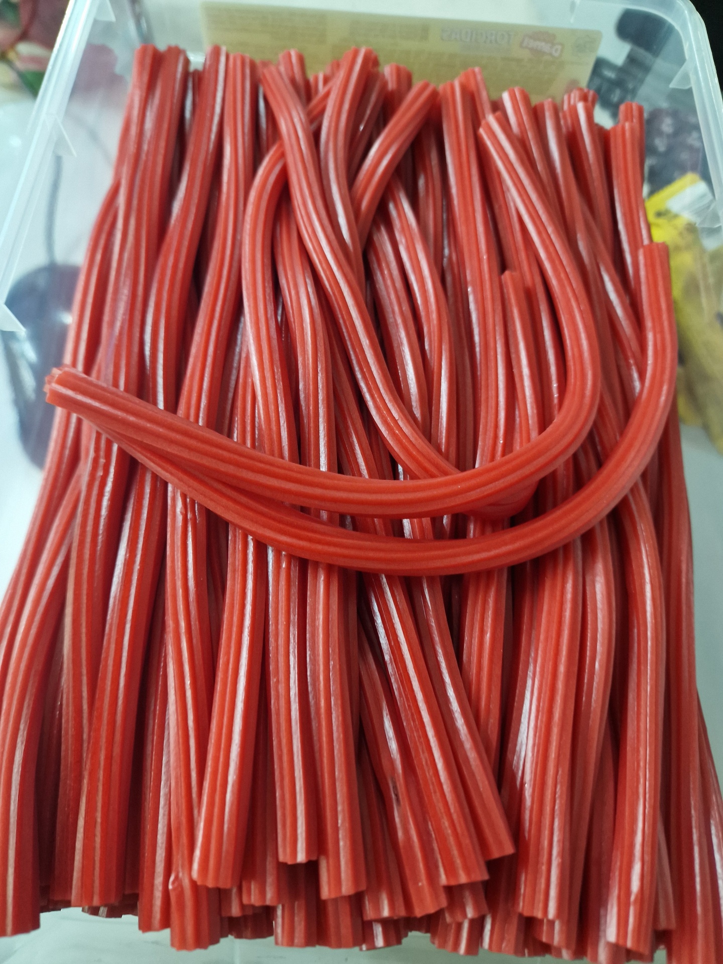 Doce vermelho em tubos flexíveis com riscas brancas dentro de caixa de plástico