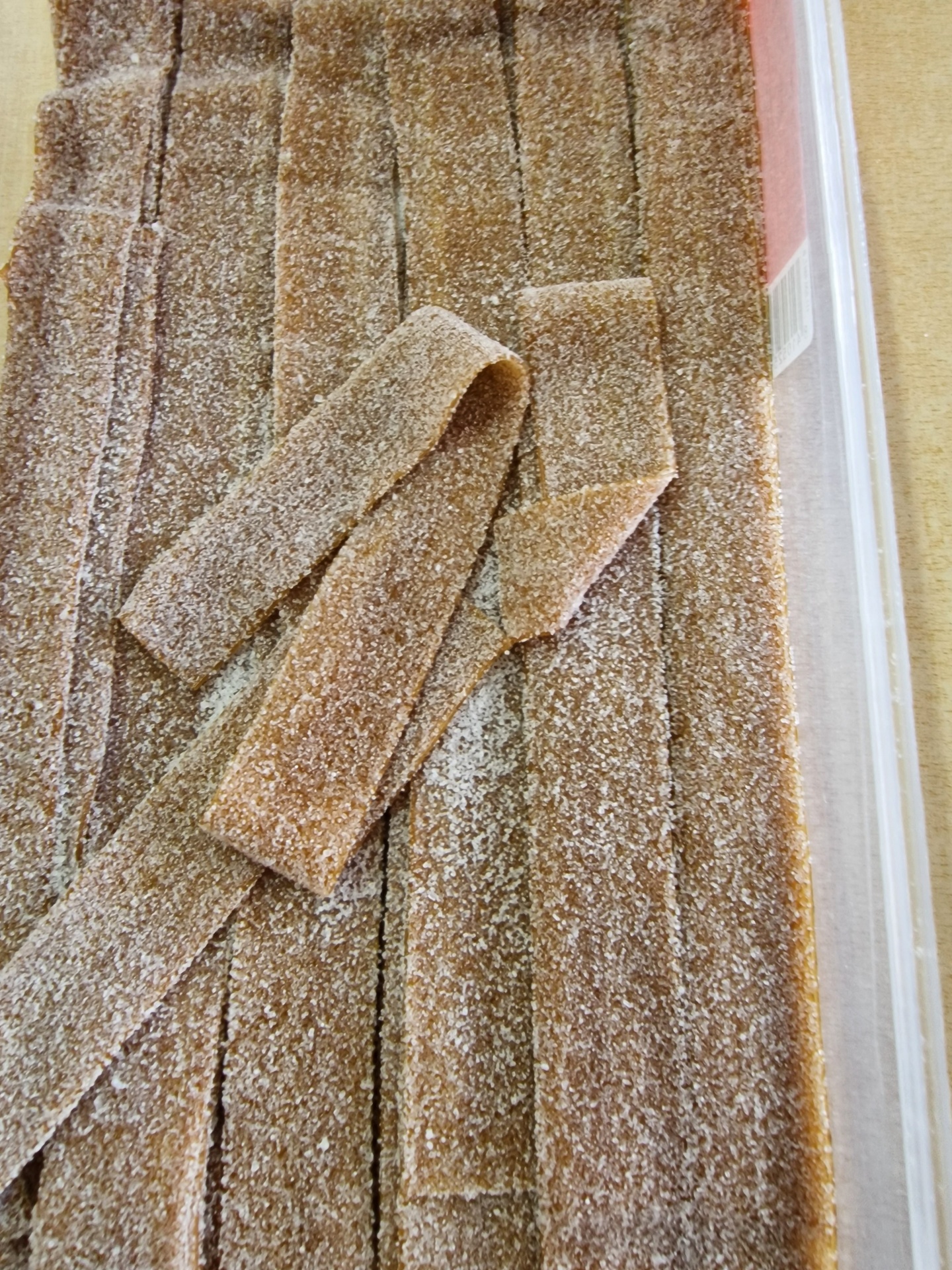 Tiras de doce castanho claro cobertas de açúcar em caixa plástica