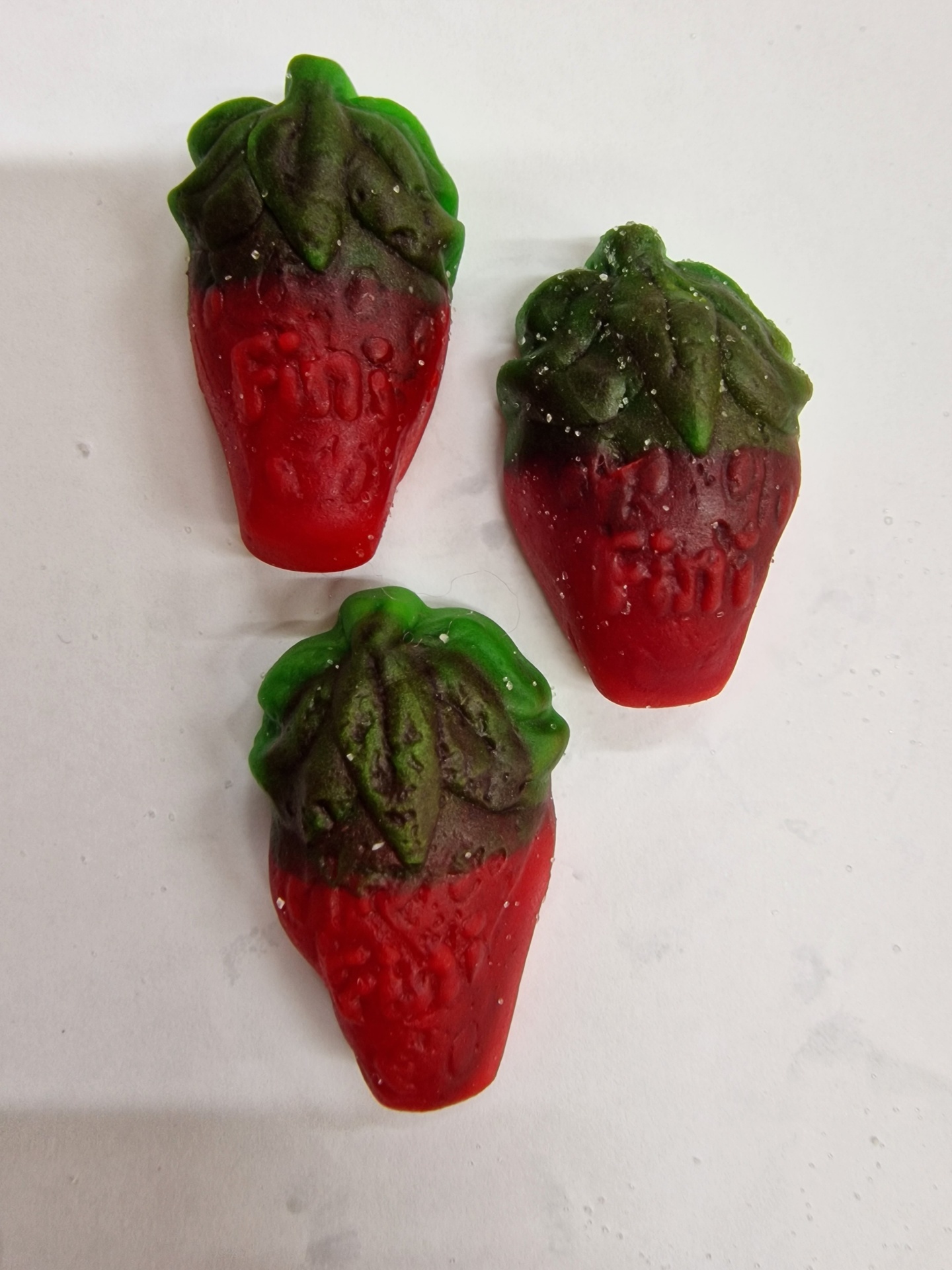 Três gomas vermelhas e verdes em forma de morango com texto em relevo