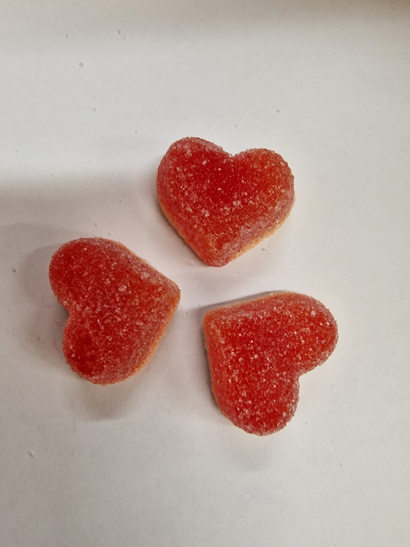 Três gomas vermelhas em forma de coração com açúcar em fundo branco