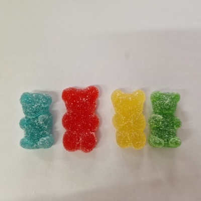 Quatro gomas em forma de ursos coloridos cobertas de açúcar sobre fundo branco