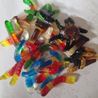 Doces de gelatina coloridos em forma de vermes e aranhas numa superfície branca
