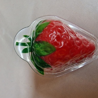 Produto em forma de morango em plástico transparente com detalhes vermelhos e verdes