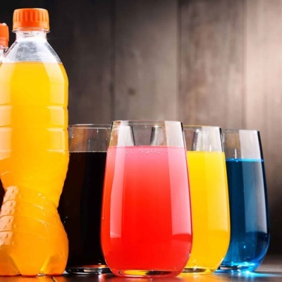 Garrafas plásticas coloridas e copos com bebidas coloridas em fundo de madeira.