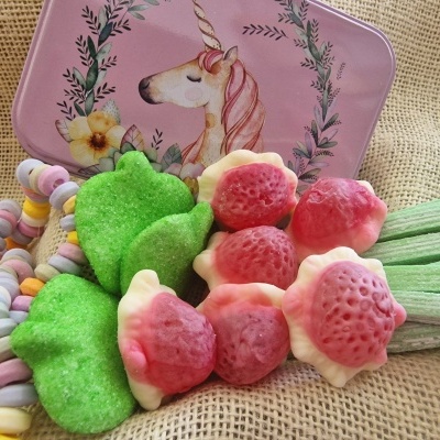 Estojo lilás com estampa de unicórnio e balas de morango, folhas verdes e doces coloridos sobre tecido bege