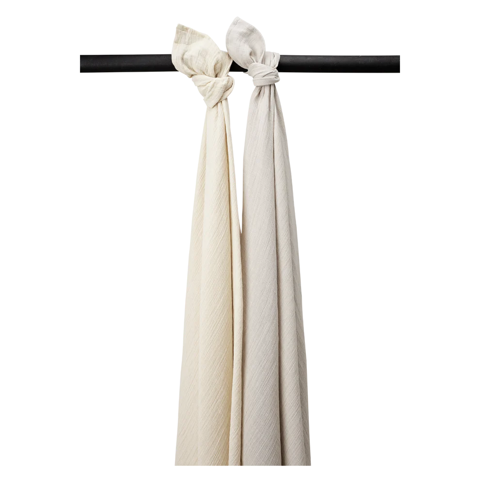Musselina Lavada Grande Pack x2 120X120cm Meuni Soft Sand/Greige | Meyco Baby Dois tecidos longos de algodão cru e bege pendurados numa barra preta