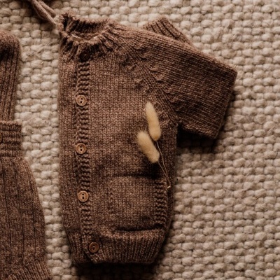 Conjunto de bebé em malha castanha com botões de madeira sobre tapete bege.