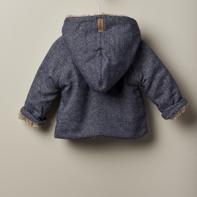 Casaco infantil cinzento com capuz forrado e bainhas de pêlo pendurado numa parede bege