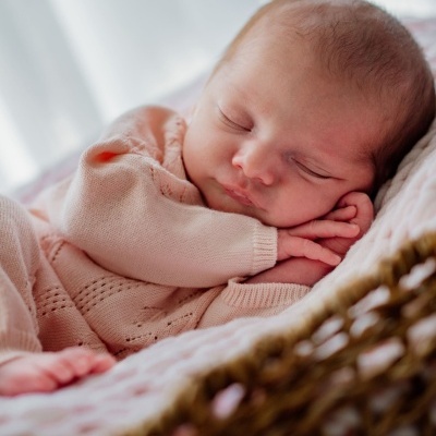 Bebé a dormir com fato de malha rosa dentro de cesta de vime com almofada cor-de-rosa