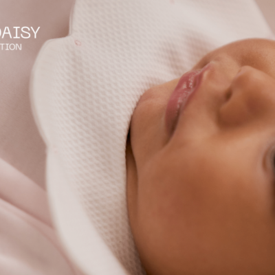 Bebé com roupa rosa e babete branco texturizado com texto DAISY COLLECTION no fundo.