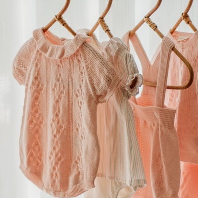 Roupas de bebé em tons rosa e listrado penduradas em cabides de madeira