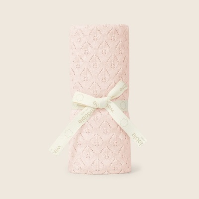 Manta rosa com padrão de folhas enrolada com fita de marca sobre fundo bege.