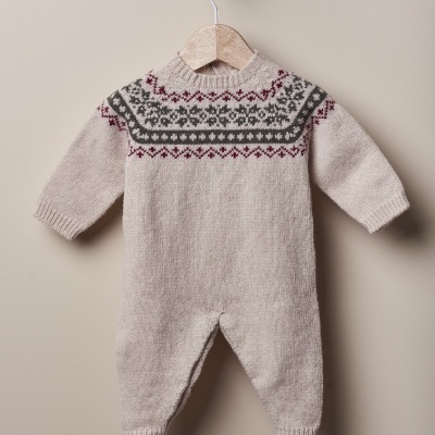 Roupa de bebé em malha bege com padrão geométrico colorido, pendurada num cabide de madeira