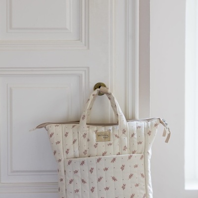Mochila acolchoada bege com padrão floral rosa pendurada numa porta branca