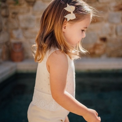 Criança pequena com roupa bege e laço no cabelo junto à piscina