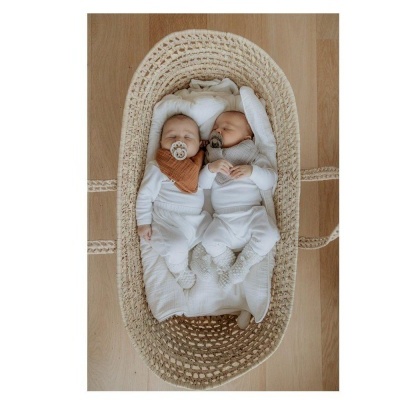 Dois bebés dormindo num berço de palha com roupa branca e bandana castanha