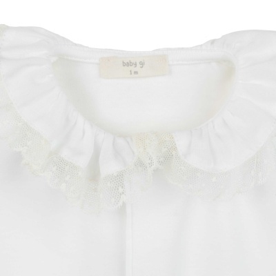 Gola de peça de roupa branca para bebé com folho de tule e etiqueta visível.