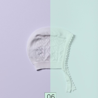 Gorro de bebé branco com fitas sobre fundo lilás e azul pastel, número 06