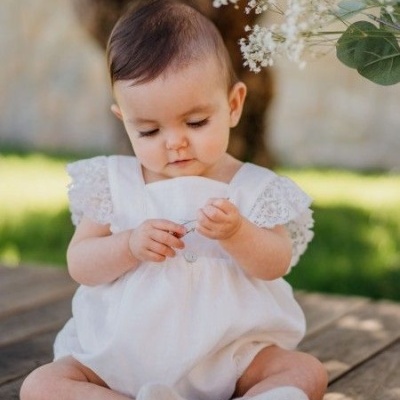 Bebé vestido branco com mangas de renda e meias brancas sentado ao ar livre