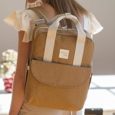 Mochila castanha de padrão de pontos brancos com alças bege numa pessoa vestida de creme