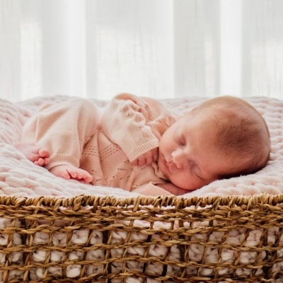 Bebé a dormir num cesto de vime com manta rosa e pijama de malha rosa