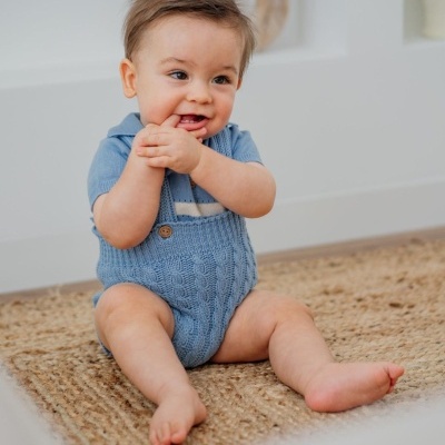 Bebé sentado em tapete castanho com roupa azul clara de malha