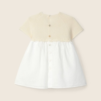 Vestido infantil bege e branco com botões atrás sobre fundo bege claro
