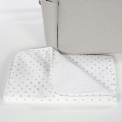 Fralda branca para bebé com padrão de corações cinzentos sobre superfície branca ao lado de mala cinzenta.