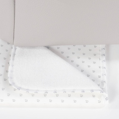 Toalha de banho para bebé branca com padrão de gotas cinzentas junto a móvel bege