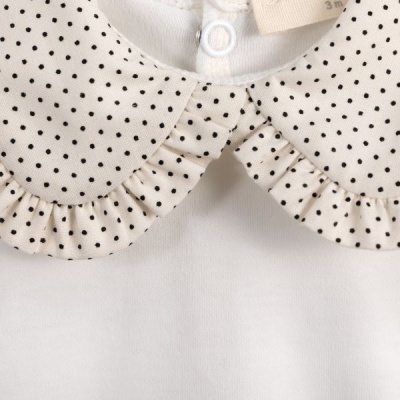 Peça de roupa branca com gola bege de pontos pretos e folhos