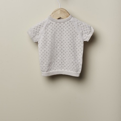 Camisola de malha bege claro em cabide de madeira numa parede bege