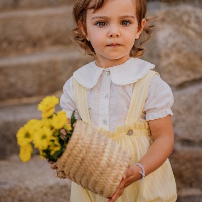 Criança com camisa branca e calção amarelo segurando cesto com flores amarelas