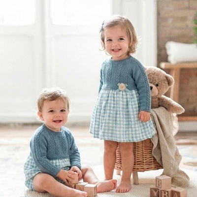 Bebés com roupa azul e padrão xadrez a brincarem com cubos de madeira em tapete creme com urso de peluche.
