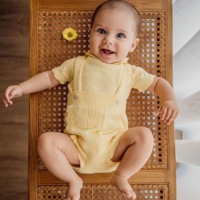 Bebé vestido de amarelo deitado numa cadeira de madeira com padrão de trama.