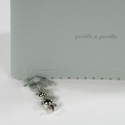 Carteira cinzenta clara com pendente de ursinho prateado e texto 'pasito a pasito'