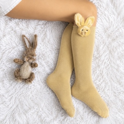 Meias amarelas com detalhes de coelho em peluche junto a um brinquedo de coelho