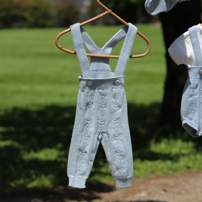 Calças de bebé azuis de malha com alças penduradas num cabide ao ar livre