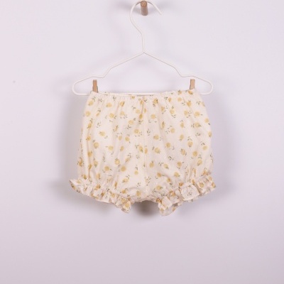 Calções de bebé brancos com padrão de flores amarelas pendurados num cabide branco