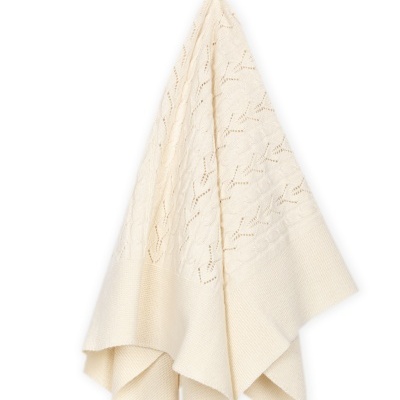 Manta creme de malha pendurada com padrão trançado e buracos decorativos.