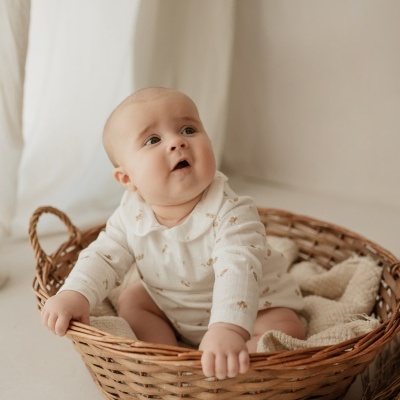 Bebé sentado numa cesta de vime com roupa clara e fundo neutro.