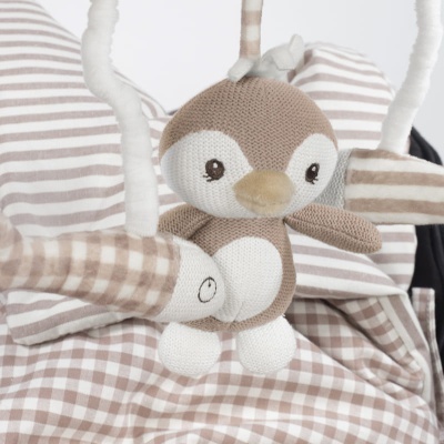 Boneco pinguim de malha castanha e branca com outros brinquedos em padrões castanhos e brancos