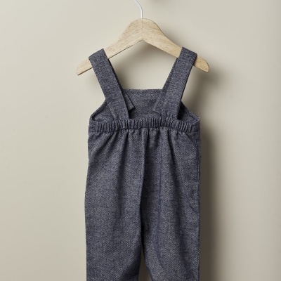 Calças cinzentas para criança com alças, penduradas num cabide de madeira.