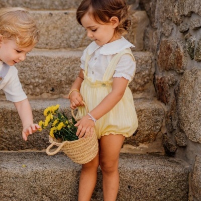 Criança com roupa amarela e branca segurando cesto de flores em escadas de pedra