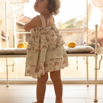 menina com vestido floral pastel e detalhes verdes numa sala com banco e limões