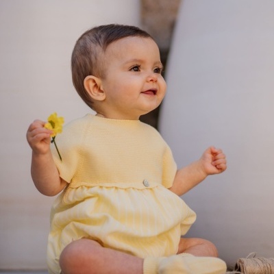 Bebé com fato de banho amarelo e meia amarela sentado a segurar uma flor amarela
