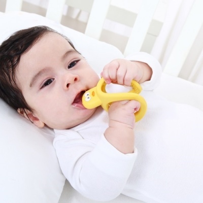 Bebé deitado de branco com mordedor amarelo em forma de banana na boca