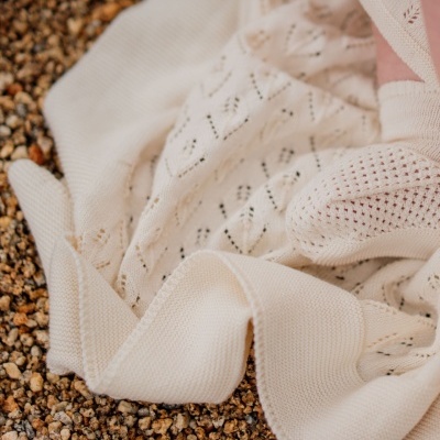 Cobertor branco de malha com padrão de losangos sobre pedras