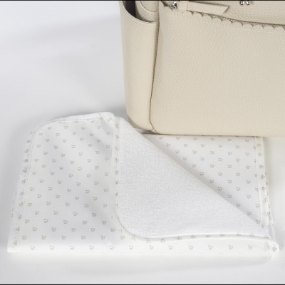 Toalha de bebé branca com padrão castanho junto a mala bege